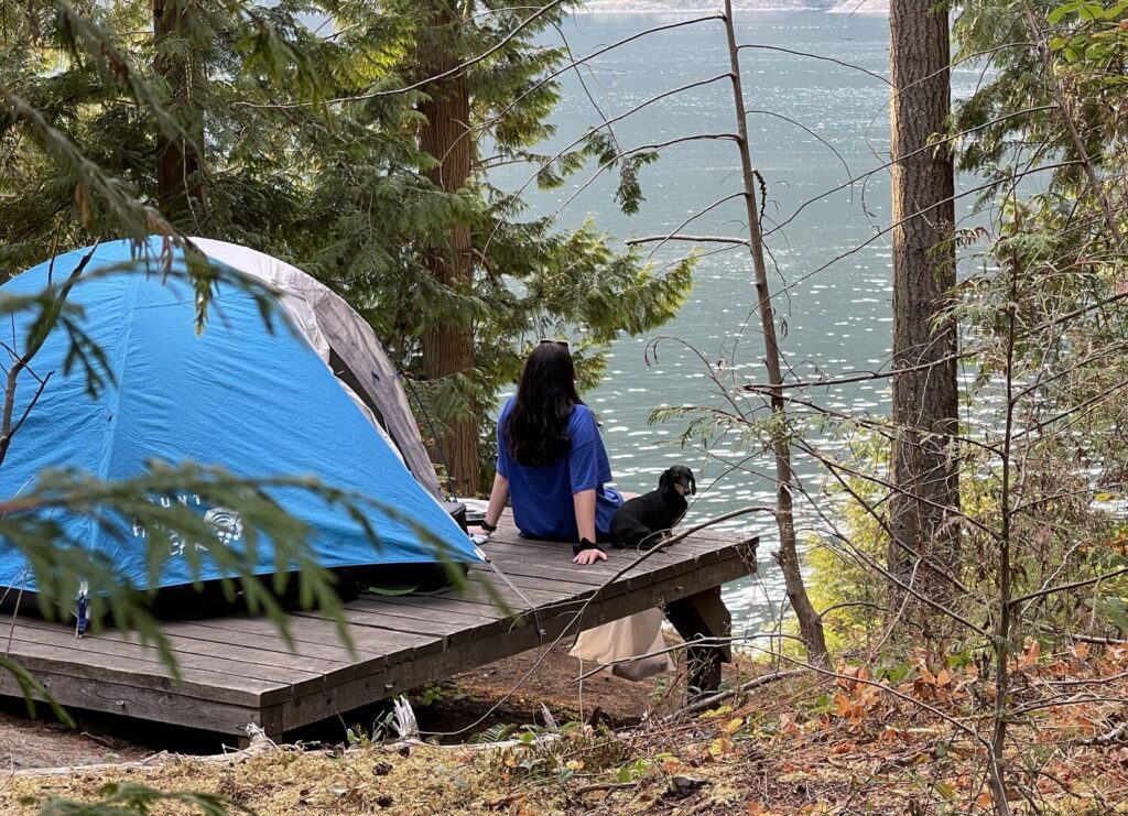 pet-friendly accommodation - young woman and dog sit by tent overlooking lake