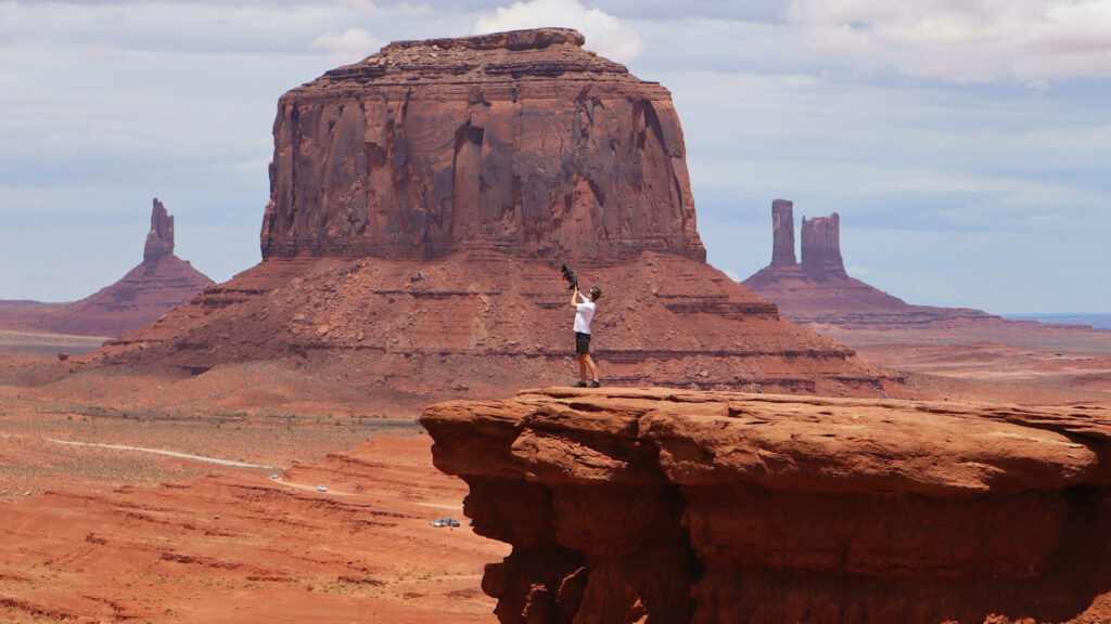 man standing on rock in front of monument valley in utah holds small dog like simba in lion king